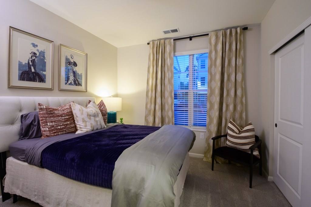 A bedroom with a bed, a chair, and two framed pictures on the wall.