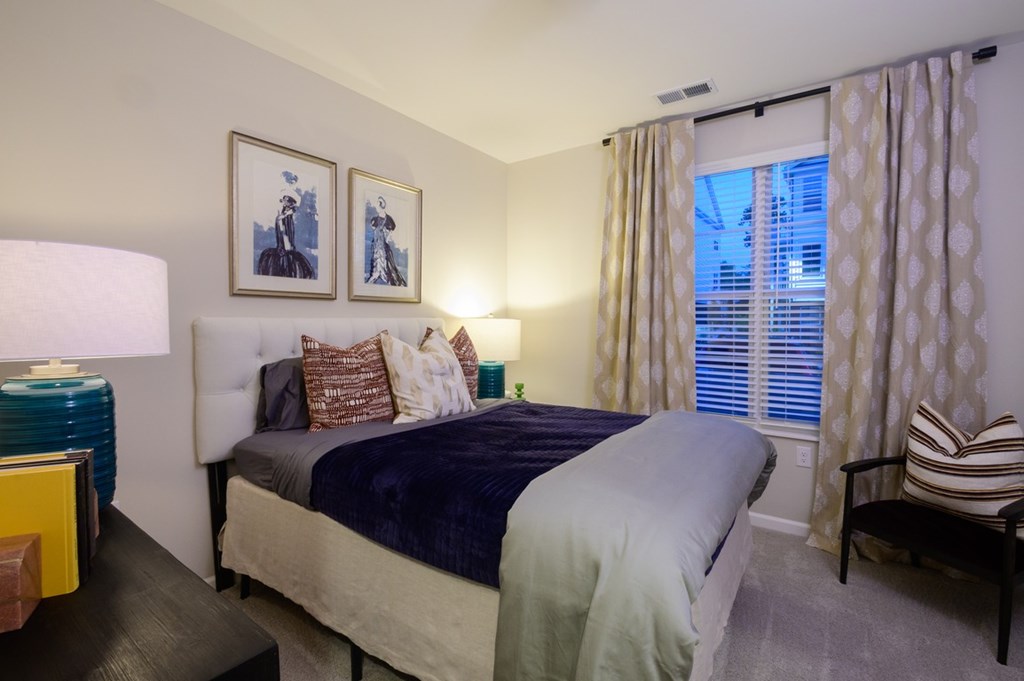 A bedroom with a bed, a chair, and two framed pictures on the wall.