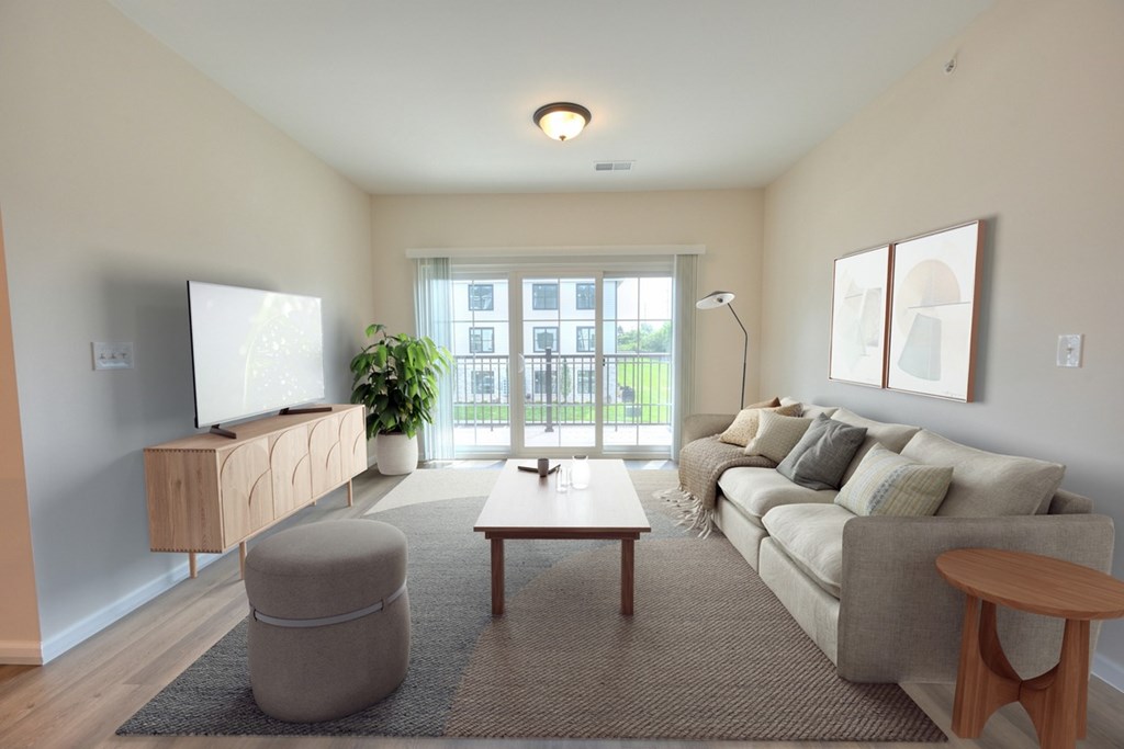 A living room with a grey sofa, a wooden coffee table, a grey ottoman, a wooden side table, a flat screen TV, a potted plant, and a window with a view of a building outside.