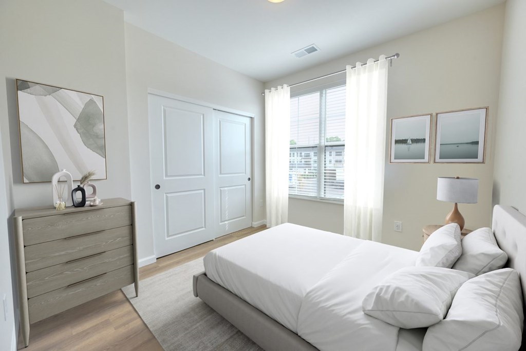 A person is lying on a bed in a bedroom with a white bedspread and a grey headboard.