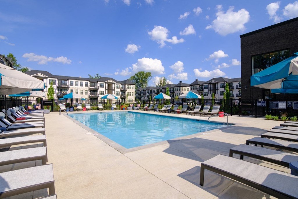 a swimming pool with lounge chairs and umbrellas in front of an apartment building at Dalton, New Albany, 43081