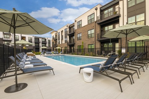 A pool area with lounge chairs and umbrellas in front of apartment buildings.
