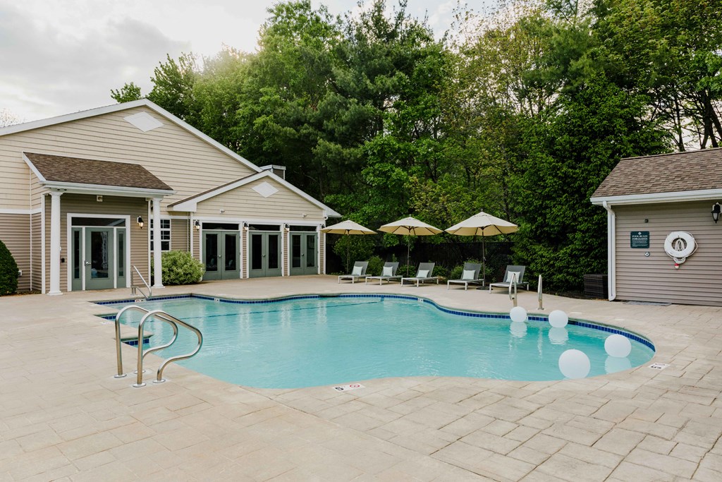 A pool with a few chairs and umbrellas in front of a house.