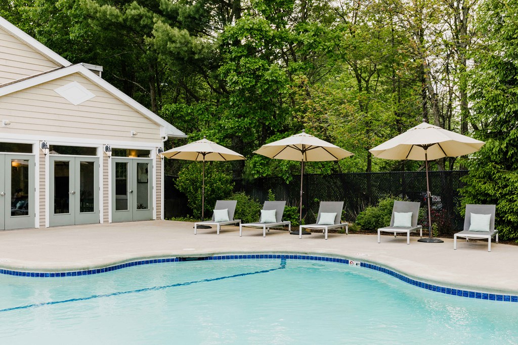 A pool with a house and four chairs with umbrellas.