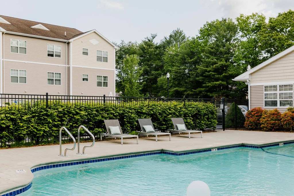 A pool with chairs and a building in the background.
