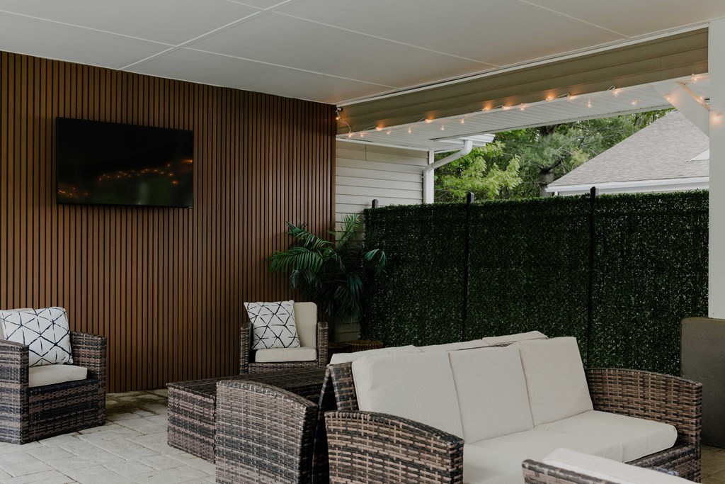 A patio with a white couch, two chairs, and a television on a wooden wall.