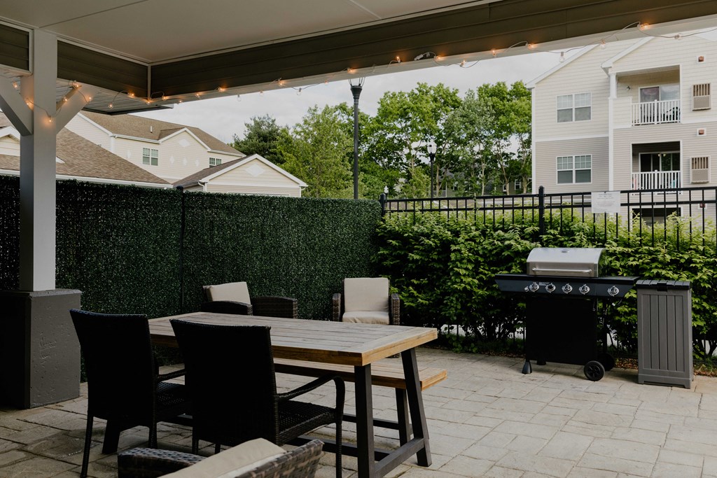 A patio with a table, chairs, and a grill.