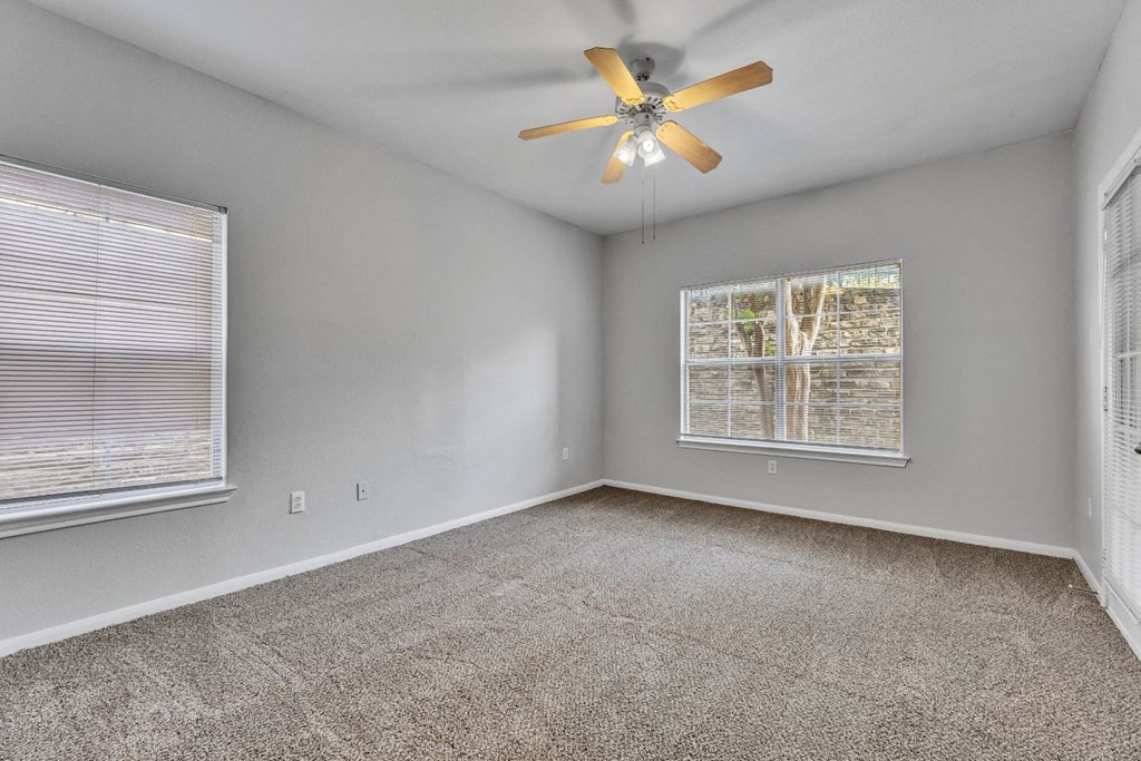 an empty living room with a ceiling fan and two windows