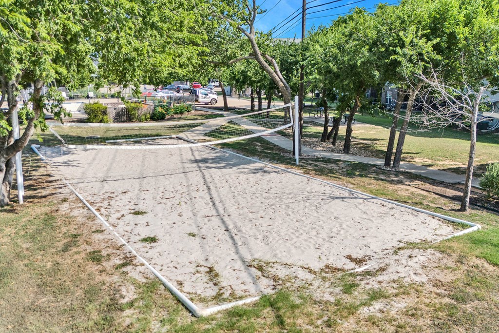 a sand volleyball court in a park with trees