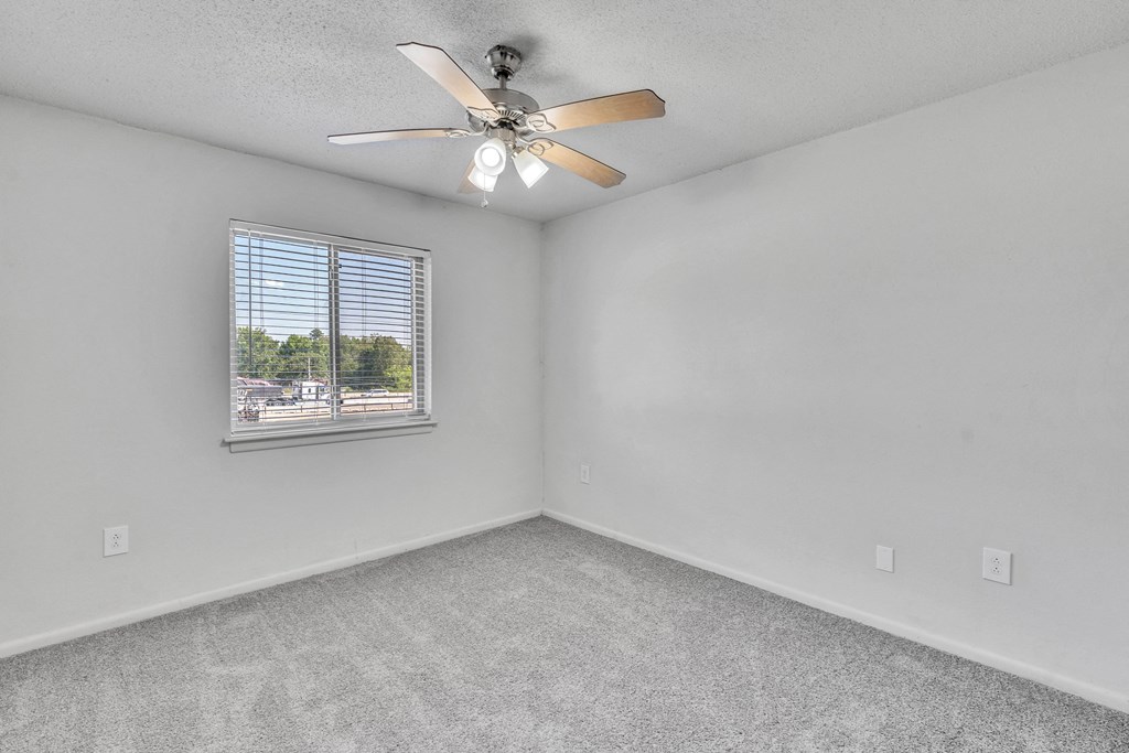 an empty bedroom with a ceiling fan and a window