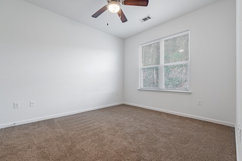A room with a ceiling fan and a window with a view of trees.