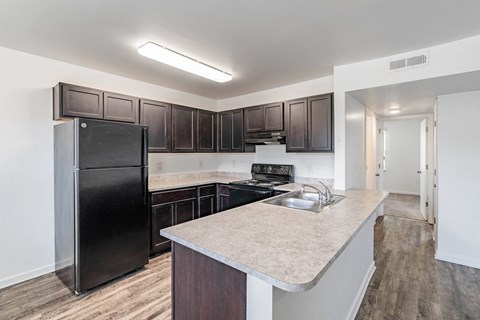 A kitchen with a black fridge and brown cabinets.
