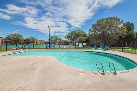 A large swimming pool surrounded by a fence and trees.