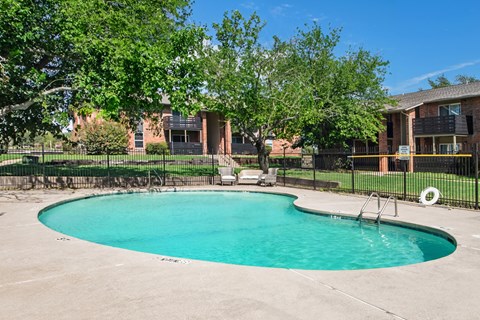 A small pool surrounded by a black fence with a tree in the background.