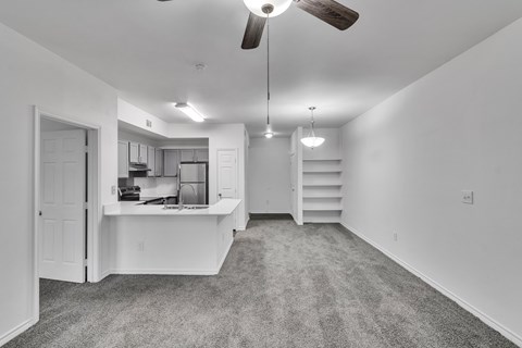 A spacious, empty room with a ceiling fan and a staircase.