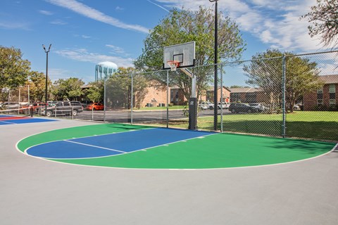 A basketball court with a green and blue surface and a basketball hoop.