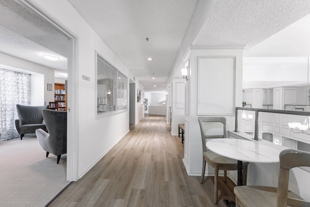 a long hallway with white walls and wooden floors and a white table and chairs