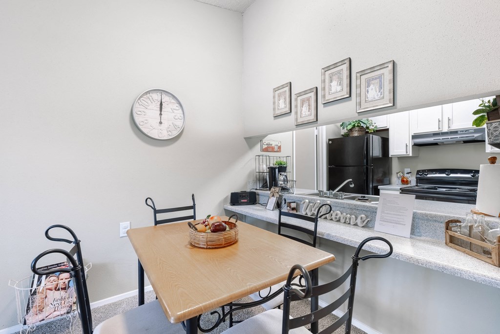 a dining room with a table and a kitchen with a clock on the wall