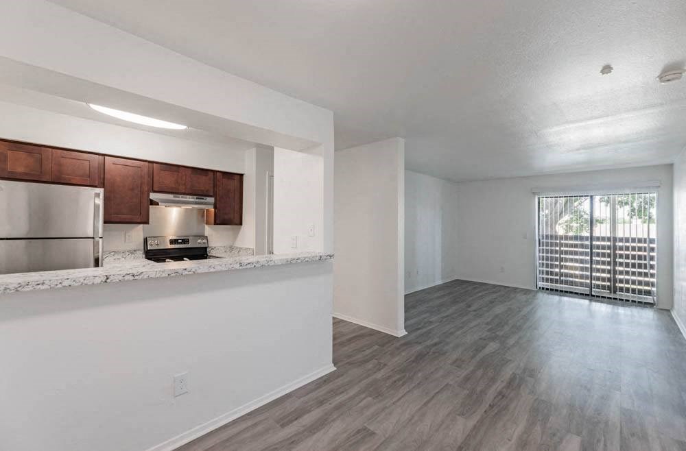 an empty living room and kitchen with a refrigerator and microwave