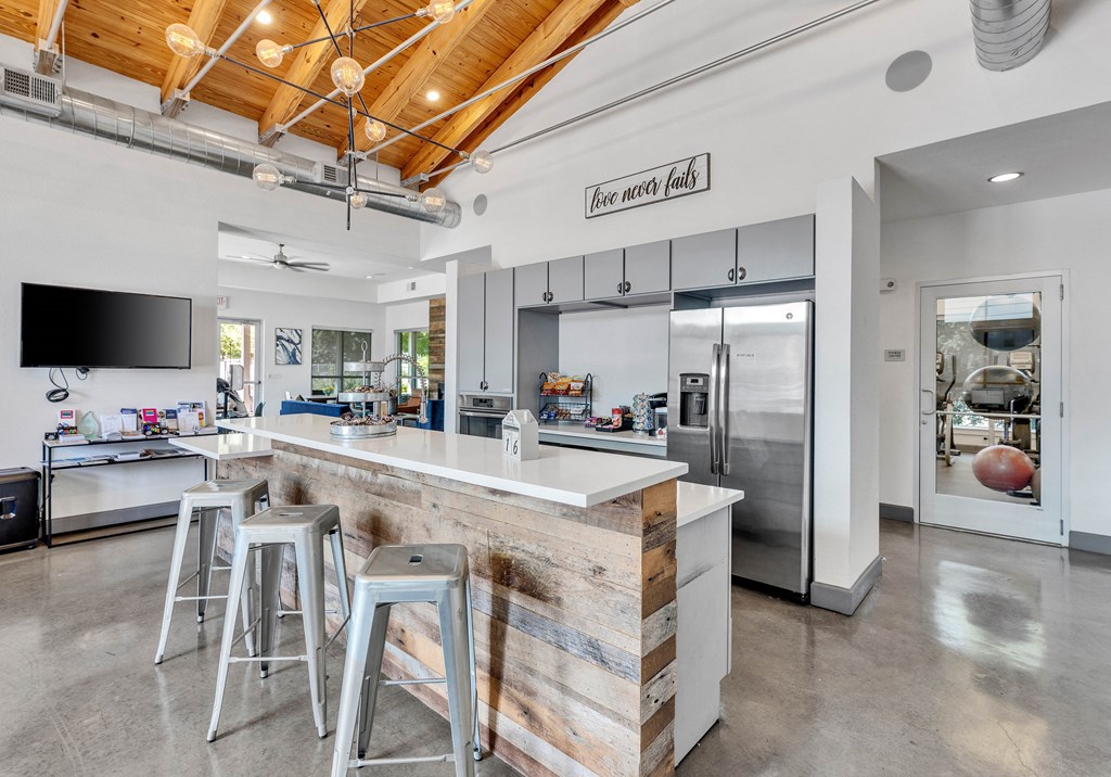 a kitchen with a bar with three stools and a stainless steel refrigerator