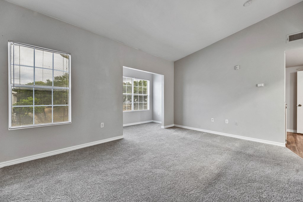 the living room of an apartment with carpet and a window