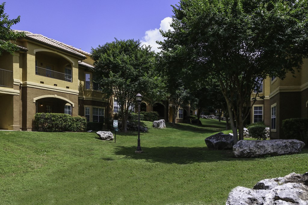 a grassy area with rocks and trees in front of apartment buildings