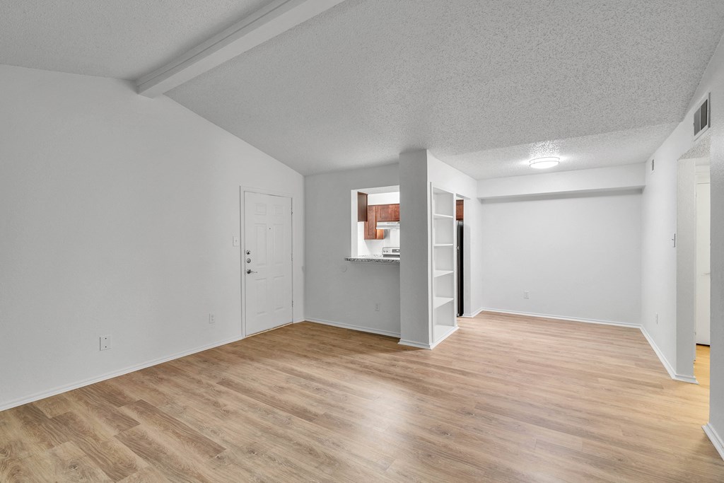 the spacious living room and kitchen with white walls and wood flooring