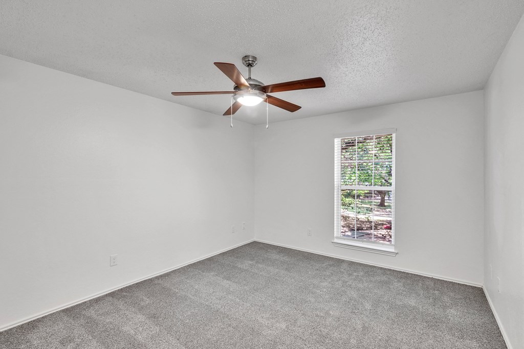 an empty living room with a ceiling fan and a window