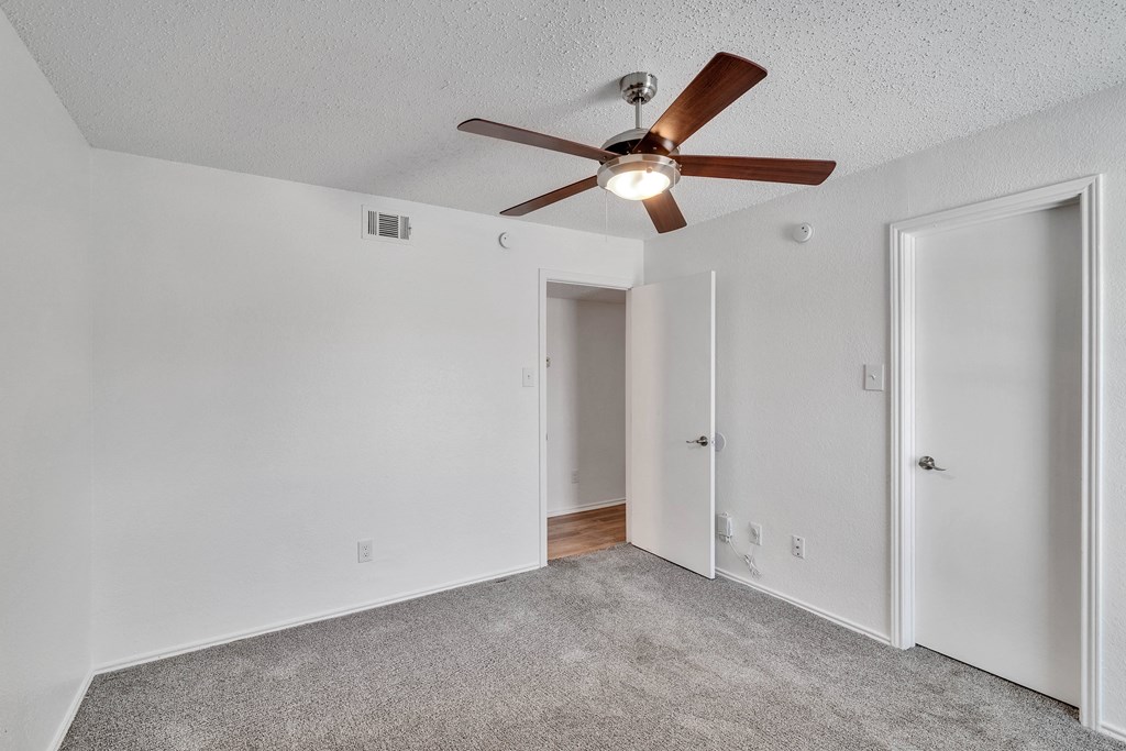 the spacious living room with ceiling fan and white walls