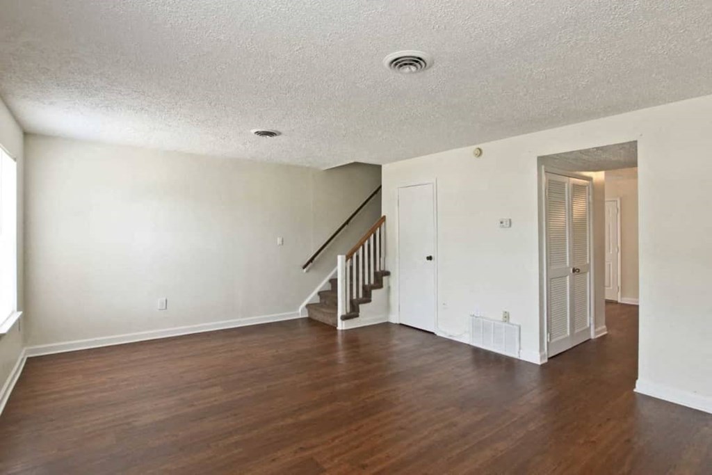 the living room and dining room of an empty house with wooden floors and a staircase
