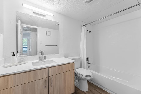A white bathroom with a sink, mirror, toilet, and bathtub.