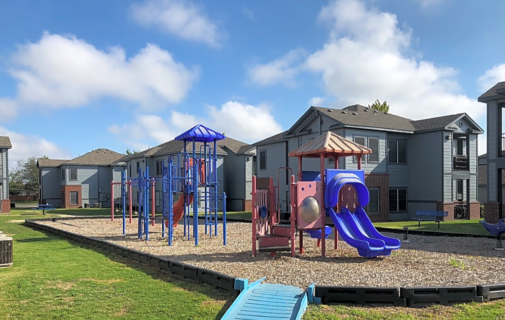 a playground with a swing set and slides in front of apartment buildings
