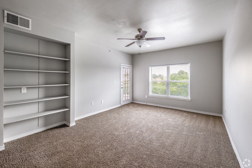 an empty living room with a ceiling fan and a window