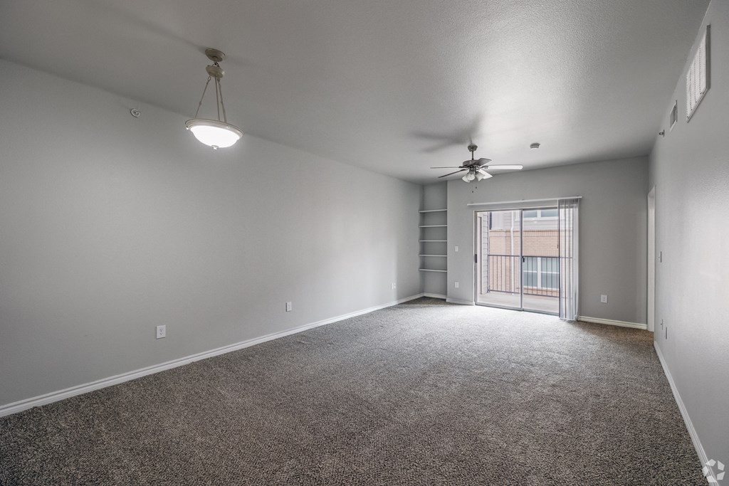 an empty living room with a ceiling fan and a door to a balcony