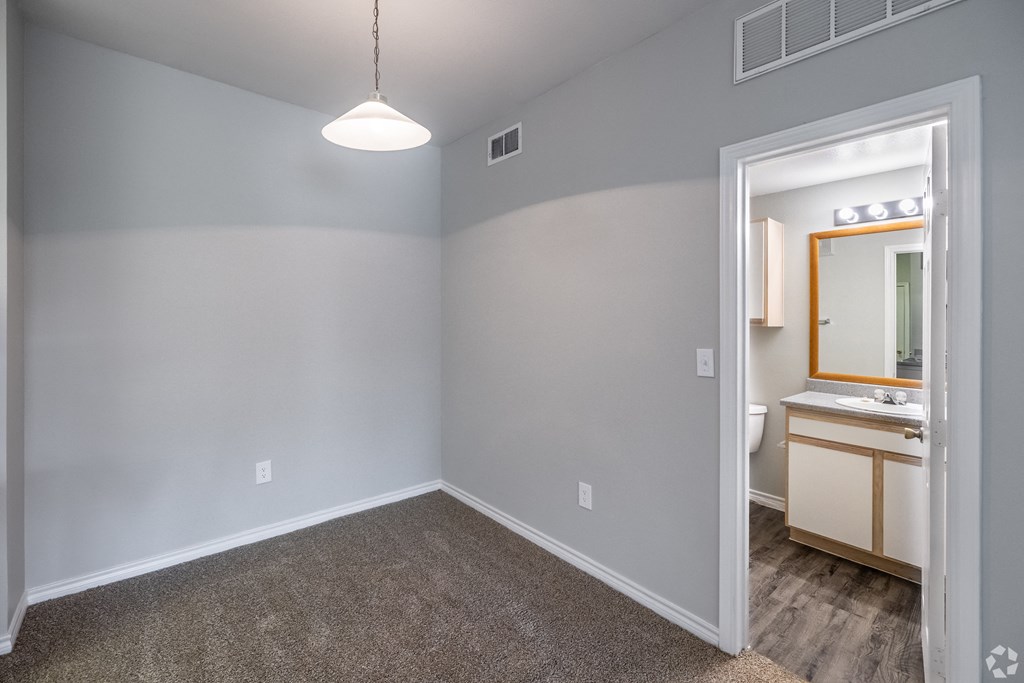 an empty bedroom with a bathroom with a sink and a mirror