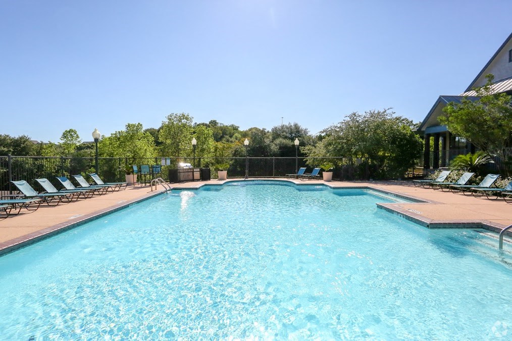 a large swimming pool with chaise lounge chairs and trees in the background