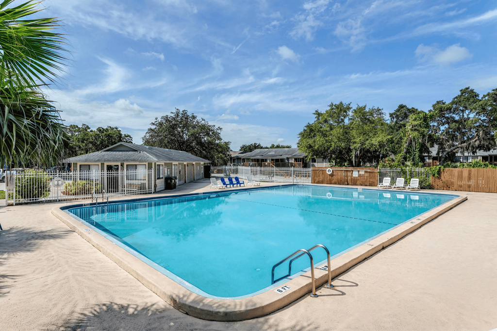 A large outdoor swimming pool surrounded by a sandy area and trees.