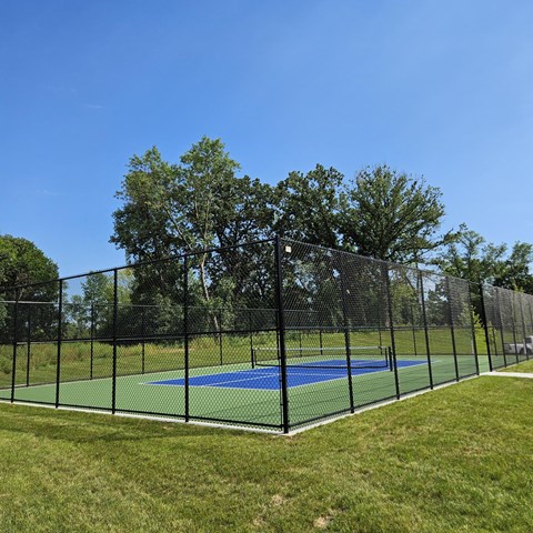 A tennis court enclosed by a black fence with trees in the background.