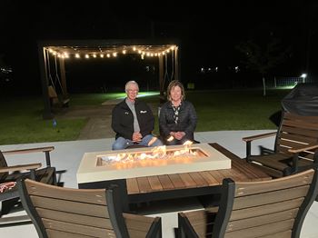 A man and a woman are sitting by a fire pit at night.