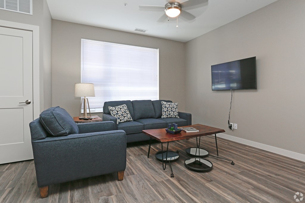 A living room with a grey couch, a wooden coffee table, and a flat screen TV mounted on the wall.