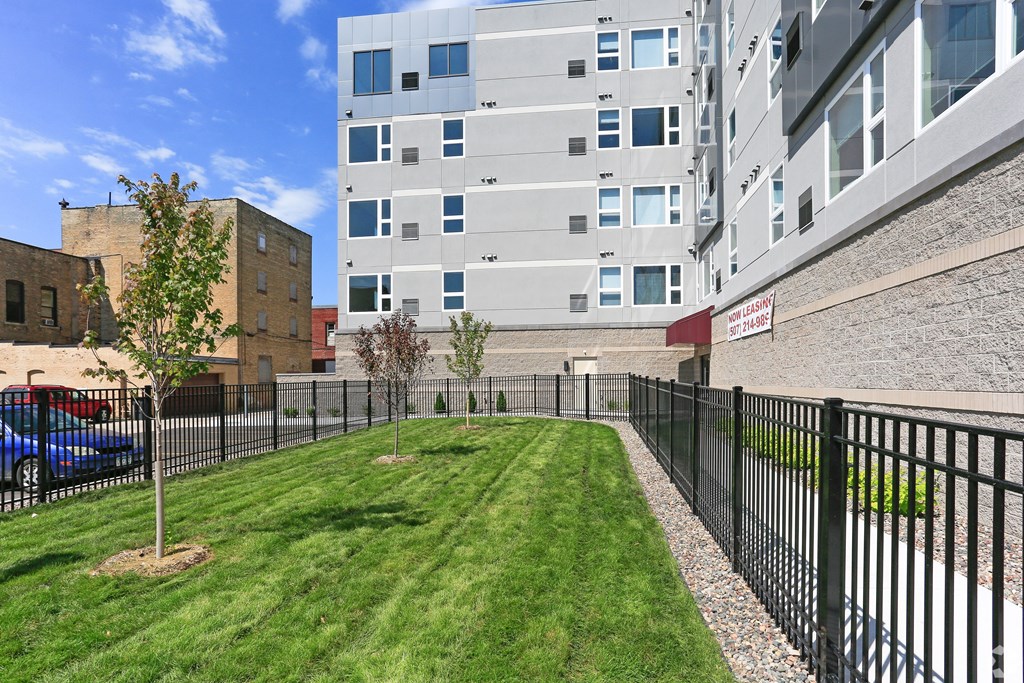 A black fence surrounds a green lawn in front of a building.