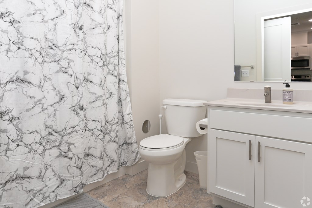 A white toilet sits in a bathroom with a marble shower curtain.