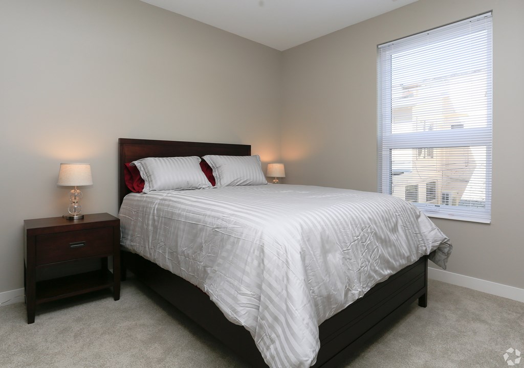 A bedroom with a bed, nightstand, and window.