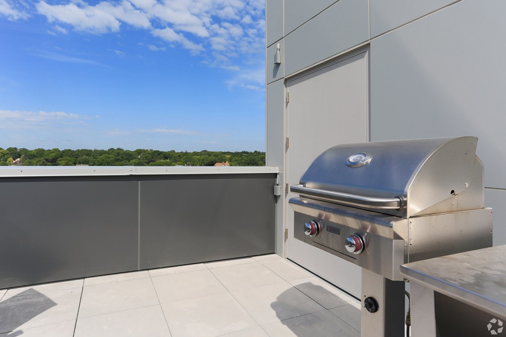 A silver barbecue grill on a patio with a view of trees and sky.