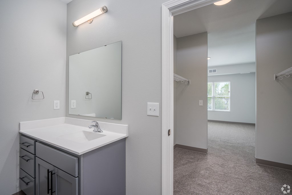 an empty bathroom with a sink and mirror and a walk in closet