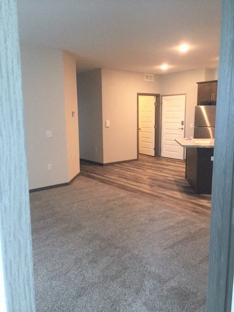 an empty living room with a kitchen and a door