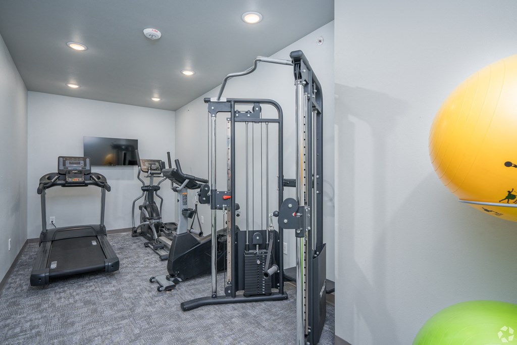 a gym with exercise equipment and a yellow ball on the floor