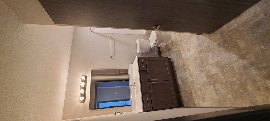 a bathroom with a brown cabinet and a window and a mirror