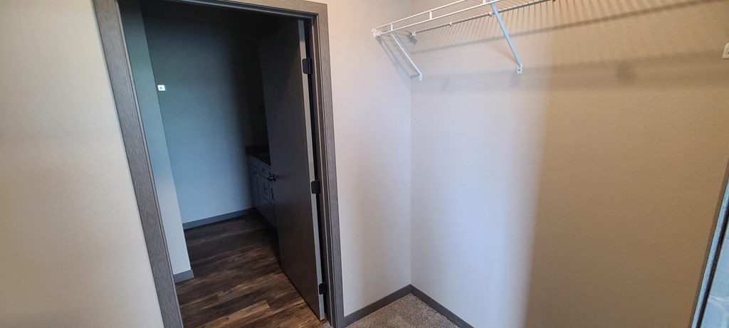 a walk in closet with a white wall and a closet door open