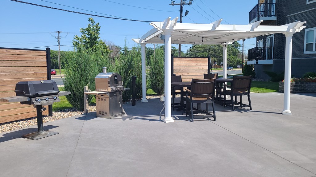 a patio with a grill and a table and chairs under a white canopy